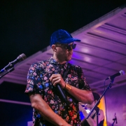 An image of the hip hop artist Decora performing in a blue baseball cap and floral button up shirt